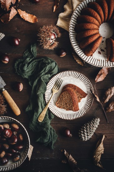A beautifully styled chestnut cake on a ceramic plate, surrounded by whole chestnuts, leaves, and