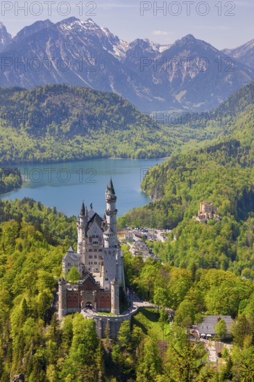 View of Neuschwanstein Castle in front of a tranquil lake and impressive mountain ranges,