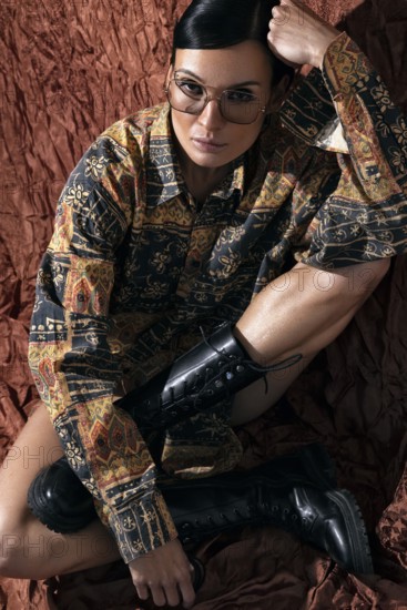 An elegant woman with slicked back hair and polarized glasses sits confidently on a textured