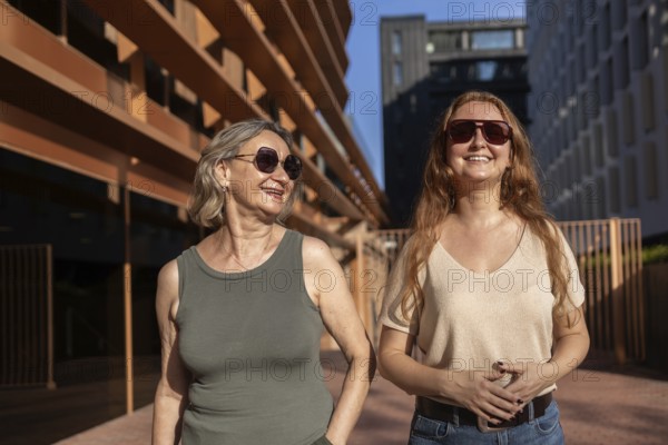 A mom and daughter share a joyful moment outdoors on a sunny day, both wearing sunglasses. The