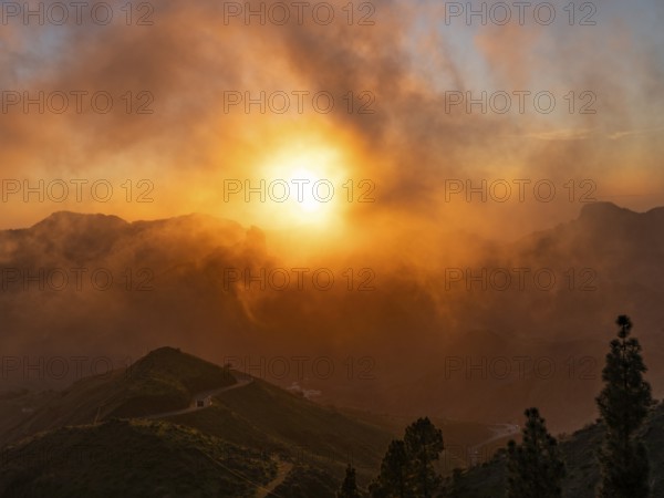 Dramatic sunset lighting up the clouds and mist over the mountains, viewed from Cruz de Tejeda in