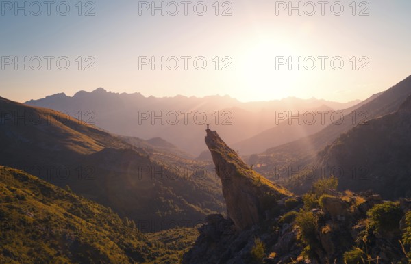 A breathtaking view of a hiker standing on a mountain peak, bathed in the golden light of a sunrise