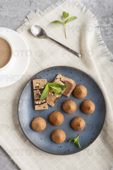 Chocolate truffle on blue ceramic plate and a cup of coffee on gray concrete background. top view