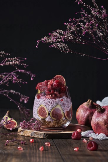 Side view of fresh fruit jam in small jar with full and cut figs on plate at black kitchen table
