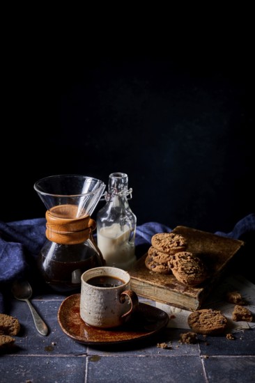 A cozy setup featuring a rustic ceramic cup of coffee, a glass bottle of milk, and a stack of