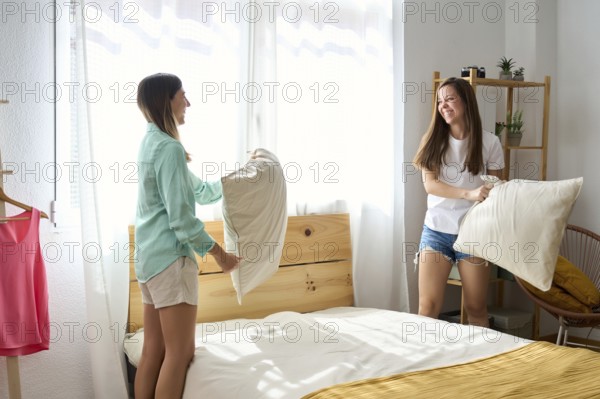 A joyful lesbian couple enjoys a playful pillow fight in a sunlit bedroom The atmosphere is filled