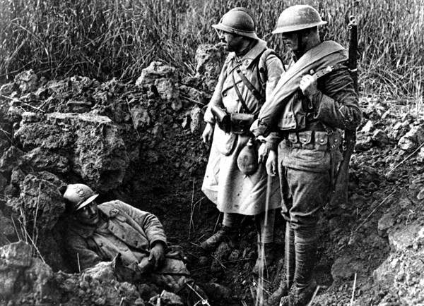 French soldier lying in a hole made by a shell and being rescued by French and American soldiers