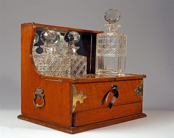 Tantalus en chêne avec trois bouteilles de cristal gravé.