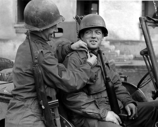 Un caporal américain aide un sous-lieutenant fraîchement nommé à mettre ses galons. (Rambervillers en France, le 2 décembre 1944)