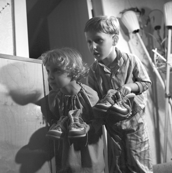 A small girl and a small boy in the pajamas carry their shoes to the door for Saint Nicholas