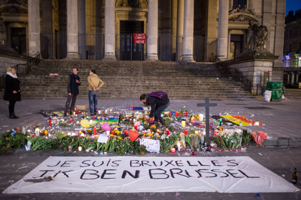 A man lights a candle behind a banner that reads 'Je suis Bruxelles Ik ben Brussel' (lit. I am