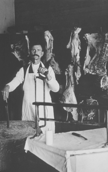 Butcher Holding Saw and Standing in Front of Hanging Meat, circa 1900