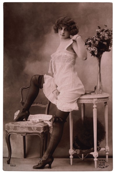French Lingerie Model Leaning on Table With One Leg Raised on Chair, 1920