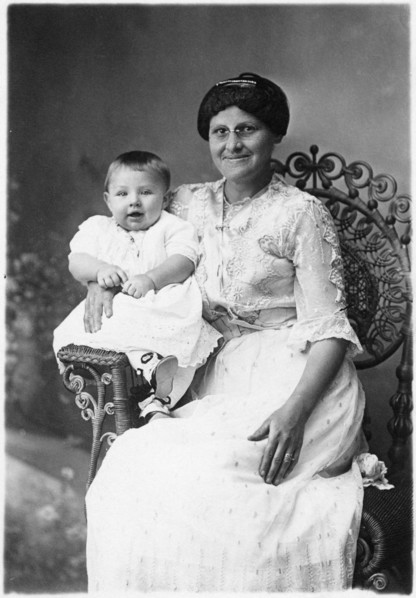 Smiling Woman Wearing Eyeglasses with Happy Infant on Arm of Wicker Chair, Portrait, circa 1920