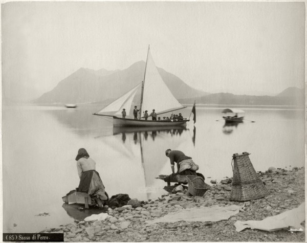 Two Women Doing Laundry at Shore of Lake Maggiore with Sailboat and Sasso di Ferro Mountain in Background, Lombardy, Italy, circa 1880