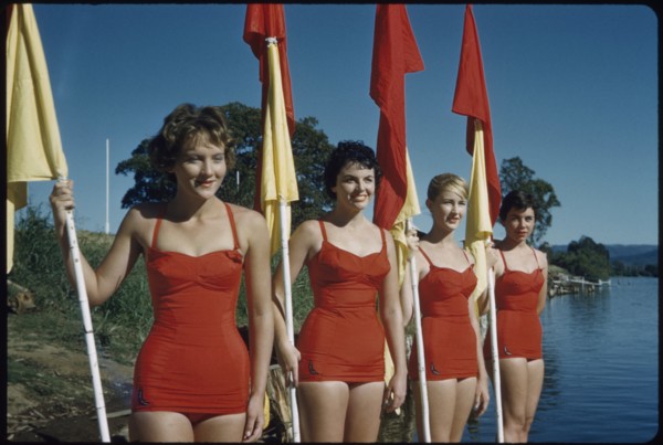 Four Young Adult Women Wearing Red One-Piece Bathing Suits and Holding Red and Yellow Flags, Australia, 1960