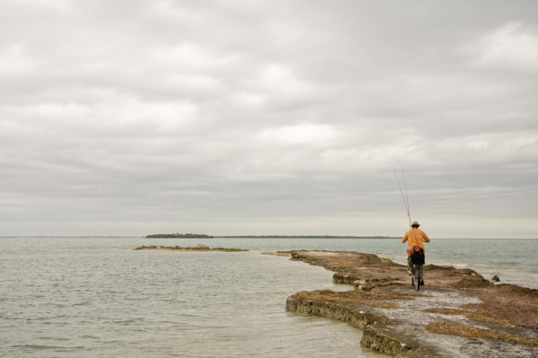 Man Riding Bicycle With Fishing Rods on Beach, Florida Keys, USA