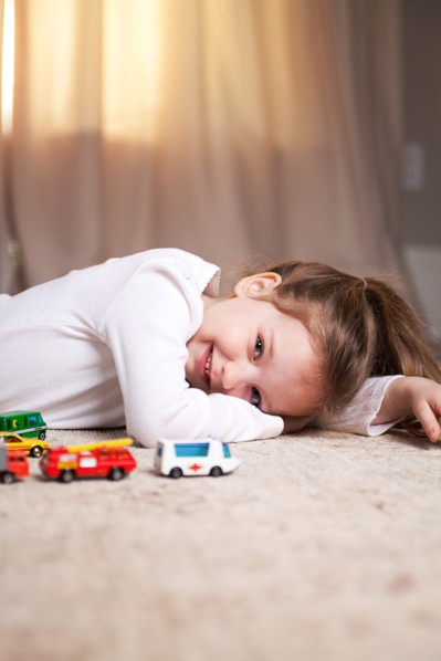 Smiling Girl Portrait on Floor with Toy Cars and Trucks