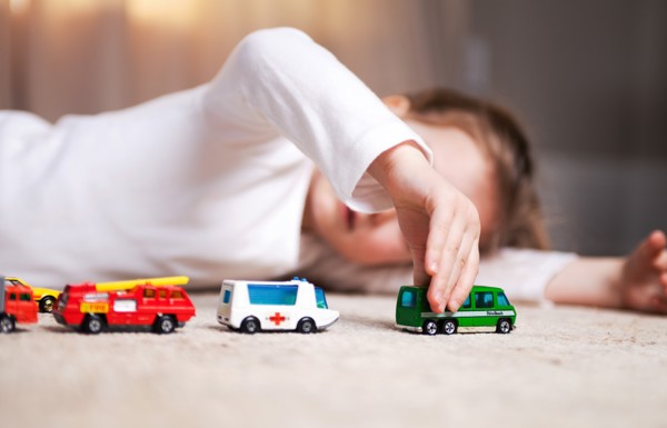 Young Girl Laying on Floor and Playing with Toy Cars and Trucks