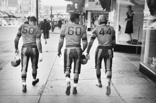 Rear View of Three High School Football Players in Uniforms walking down Street