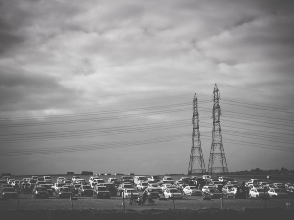 Multiple Cars Parked in Field with Electric Pylons in Background