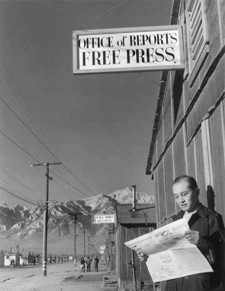 Editor Roy Takeno reading Copy of Manzanar Free Press in front of Newspaper Office