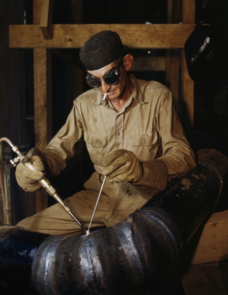 Welder gas welding a joint in a line of spiral pipe