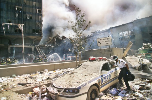 Rescue worker reaching into a New York Police car covered with debris with smoldering ruins in background