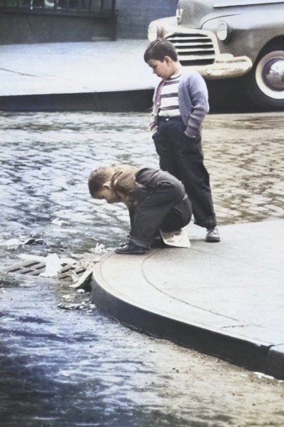 Two Young Boys on Street Corner looking in Storm Drain