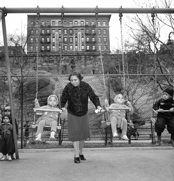 Woman pushing young children on swings at urban playground