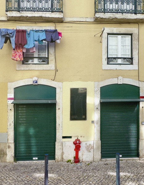 Clothes hanging on line on building facade above two shuttered green doors, Lisbon, Portugal