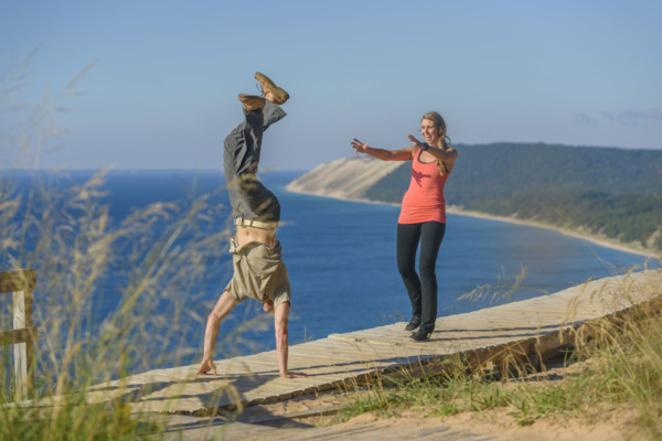 Young adult man performing handstand while young adult woman watches with arms extended forward