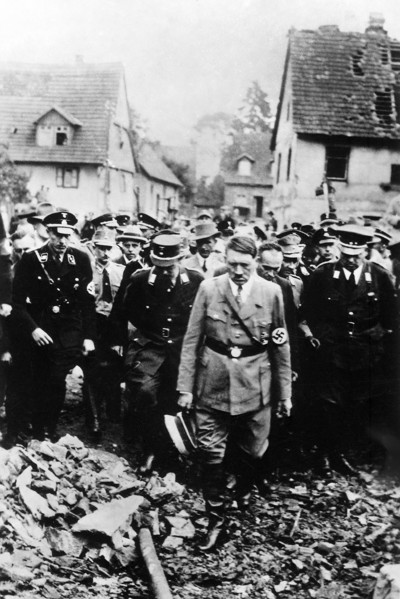 Adolf Hitler, accompanied by other German officials, grimly inspecting bomb damage in German city,