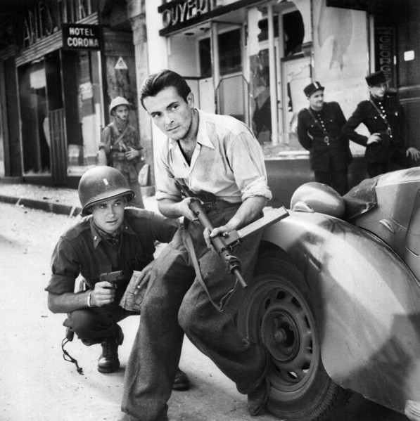 American officer and French partisan crouch behind an auto during a street fight, France, U.S. Army
