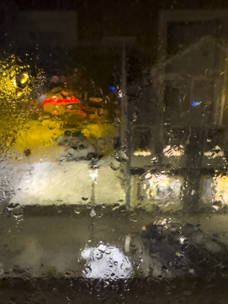 Blurred street scene viewed through window with dripping raindrops at night