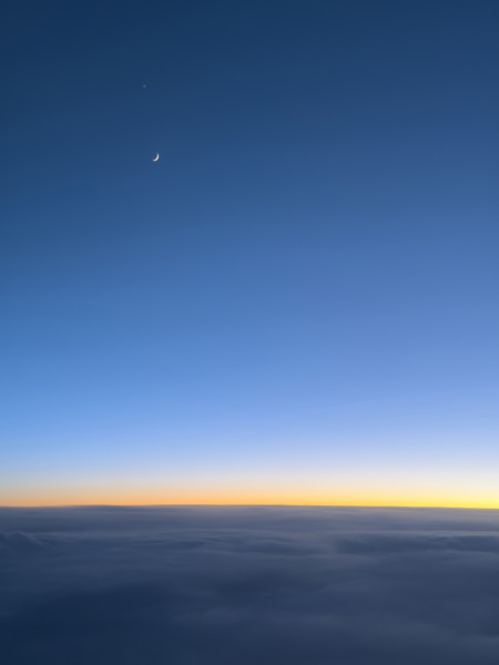 Crescent moon in deep blue sky at sunset viewed through airplane window