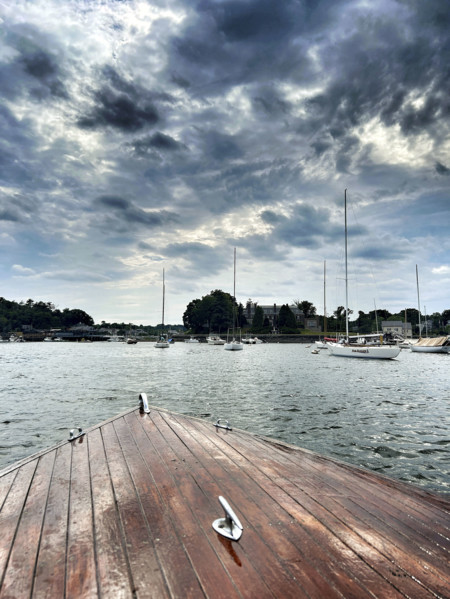 Bow of vintage wood boat with moored harbor sailboats in background