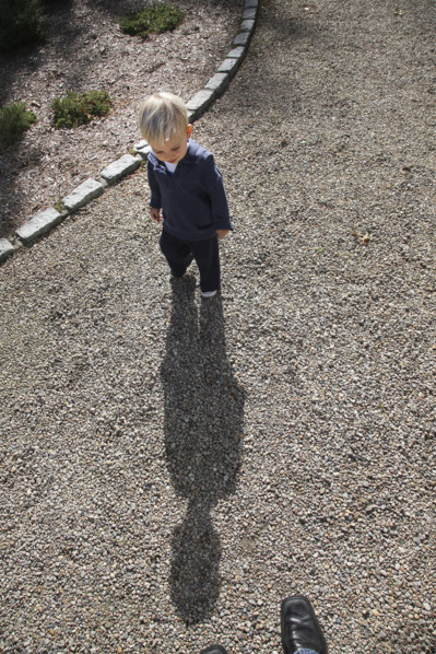 High angle view of young boy casting long shadow on gravel driveway