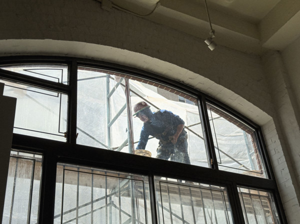 Construction worker repairing building façade, viewed through residential apartment window,