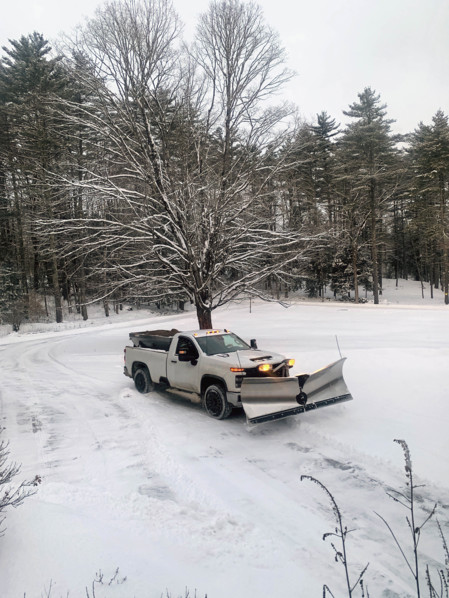 White pickup truck with plow attachment removing snow from residential driveway