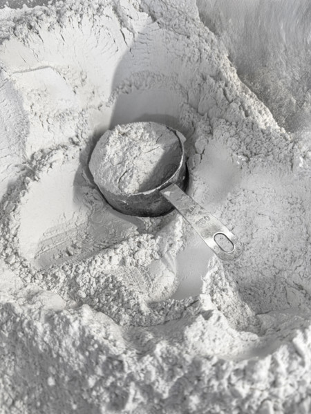 Full measuring cup of flour sitting in a mound of flour