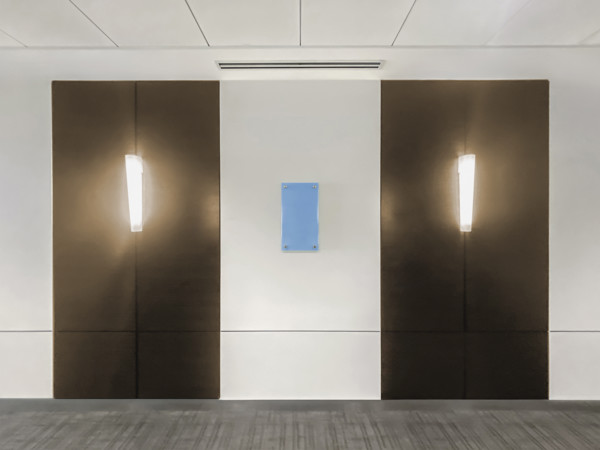 Two light fixtures mounted on hallway wall in office building