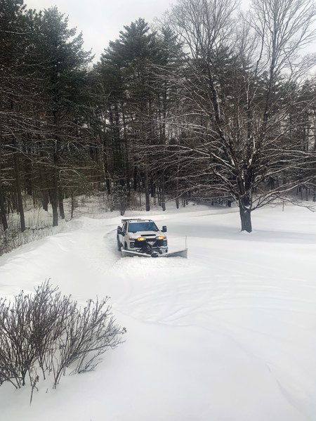 White pickup truck with plow attachment removing snow from residential driveway