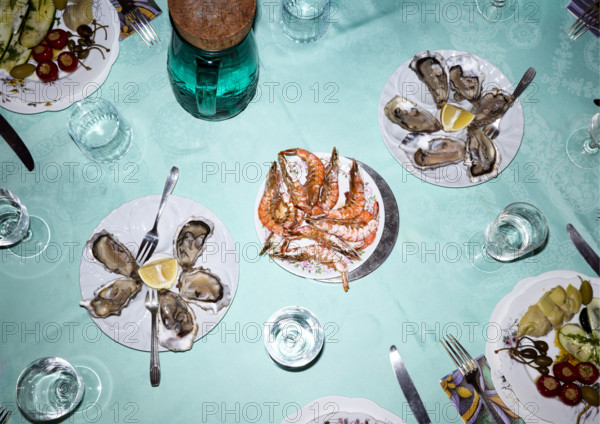 High angle view of dining table featuring plates of oysters and prawns with glasses of water and