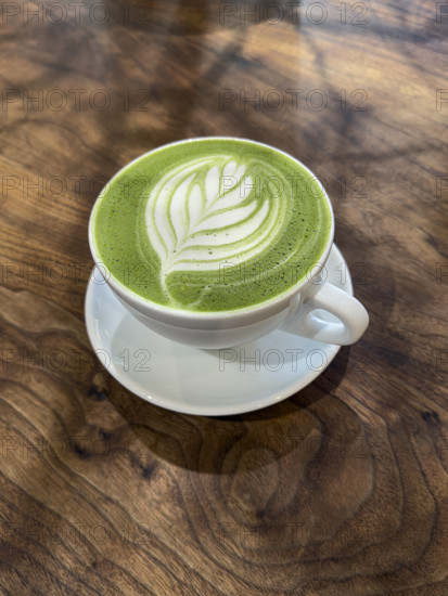 High angle view of cup of matcha green tea latte on wood-grained table