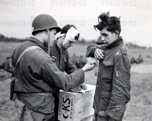 American soldier making out identity tag for young German prisoner of war as another wounded Nazi