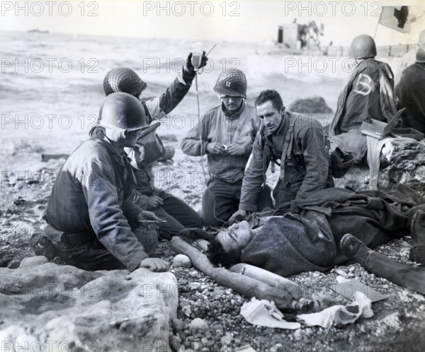 U.S. Army medical soldiers, just a few feet from the surf, administering plasma transfusion to