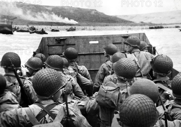 American assault troops in landing craft huddling behind protective front of craft as it nears