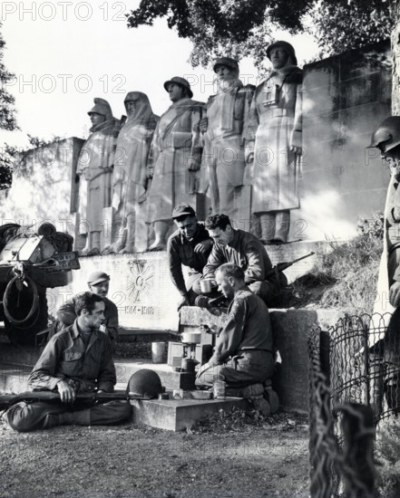 Group of American soldiers cooking dinner on GI stove under World War I memorial, near Verdun,
