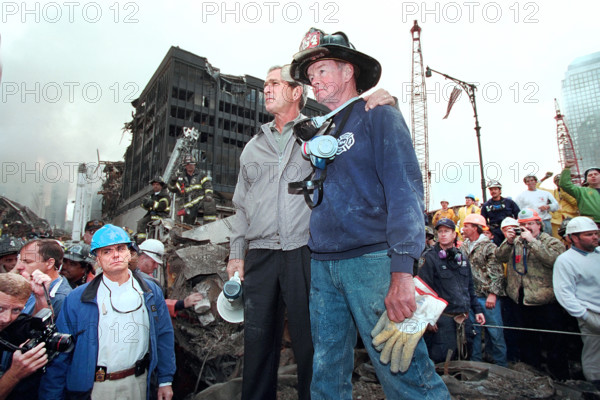 U.S. President George W. Bush standing atop burned out emergency vehicle with retired New York City